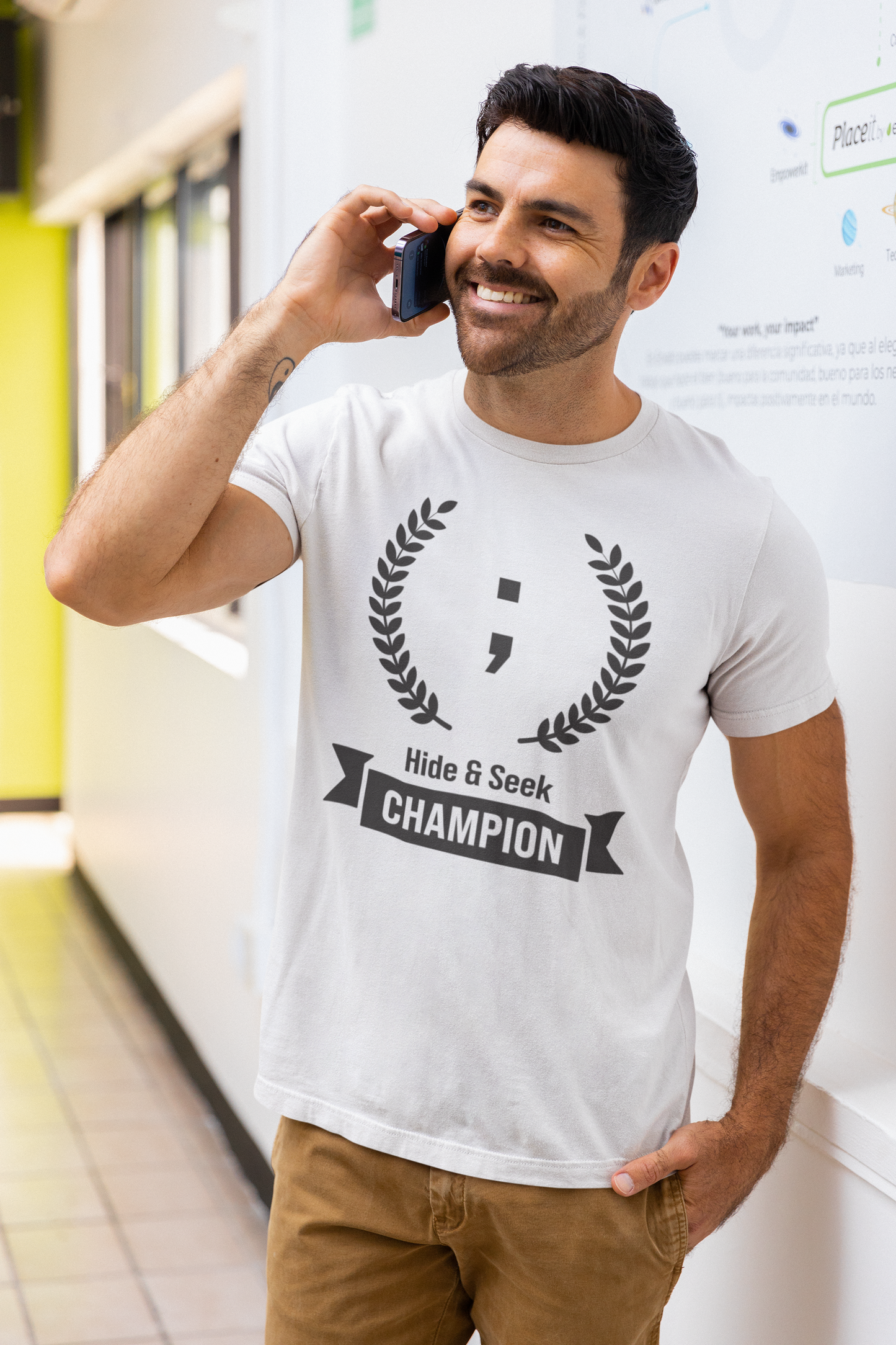 A man talking on the phone wearing a white programming t-shirt with the text Hide & Seek Champion, featuring a semicolon.