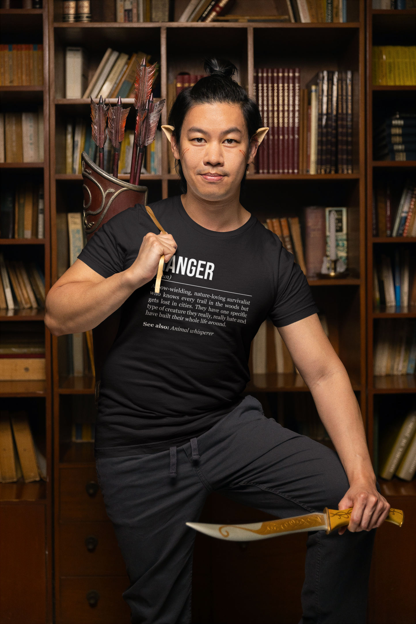 A standing man with elf ears carrying a quiver with arrows and holding a dager, wearing a black ranger T-shirt showing the definition of the class Ranger.
