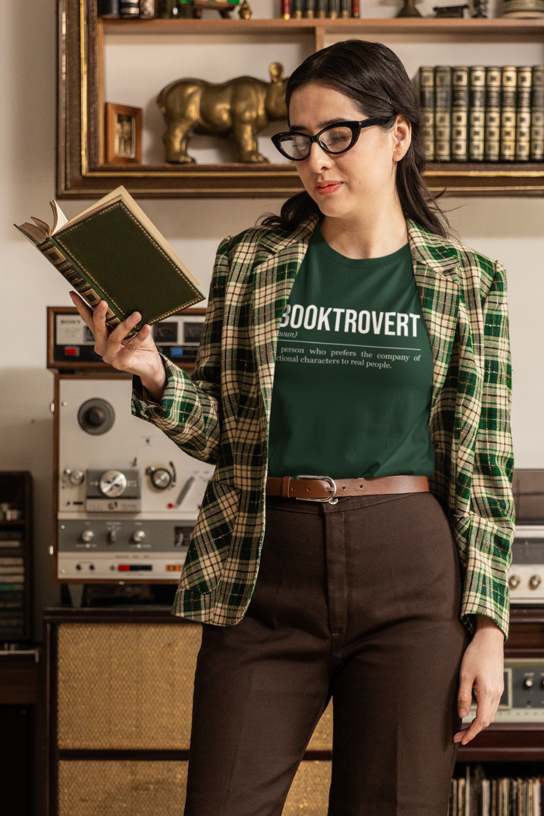 A nerdy girl reading a book and wearing a forest green book T-shirt showing the definition of the word Booktrovert.