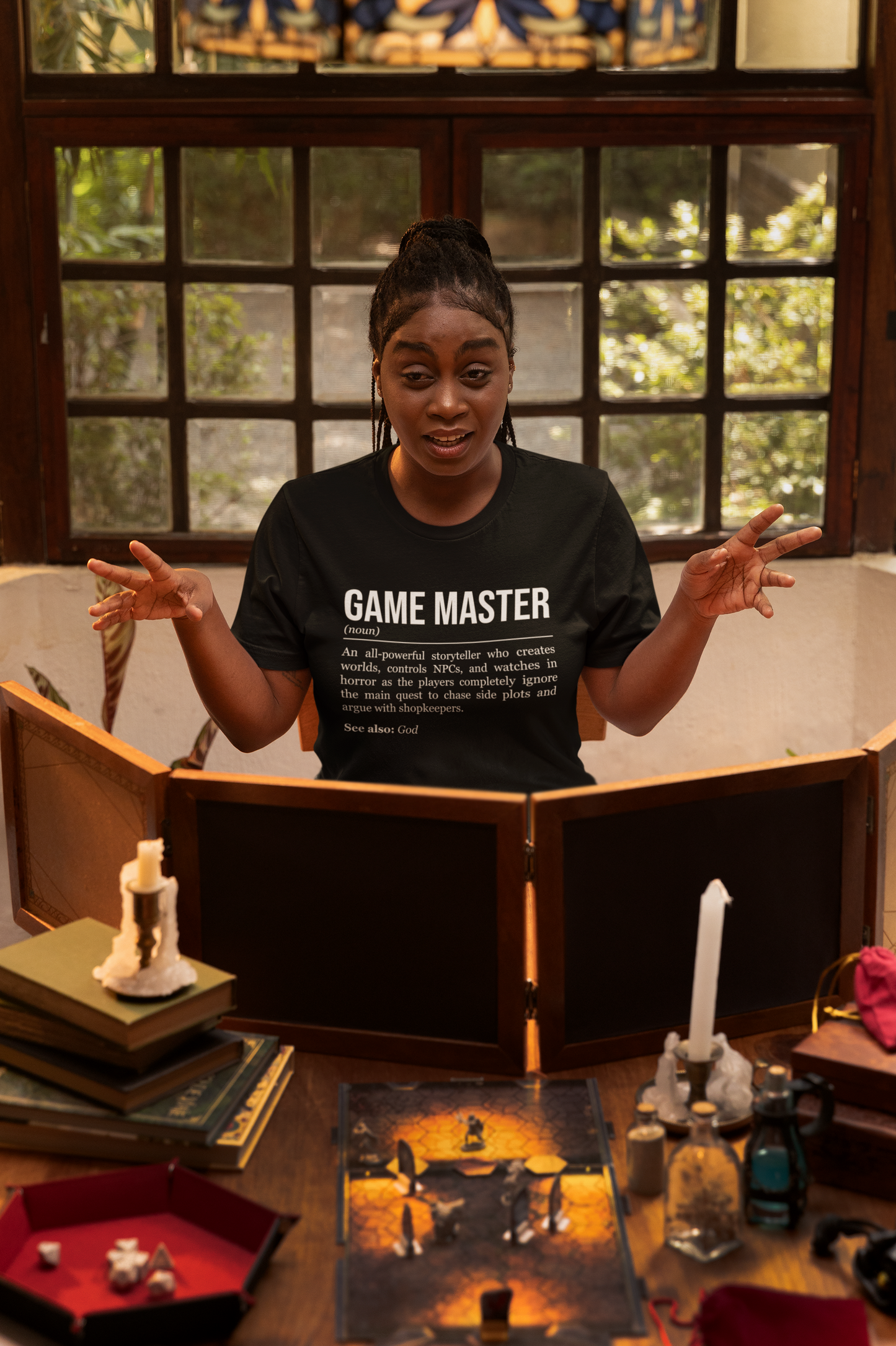 A game master behind a game master screen, wearing a black RPG T-shirt showing the definition of Game Master.