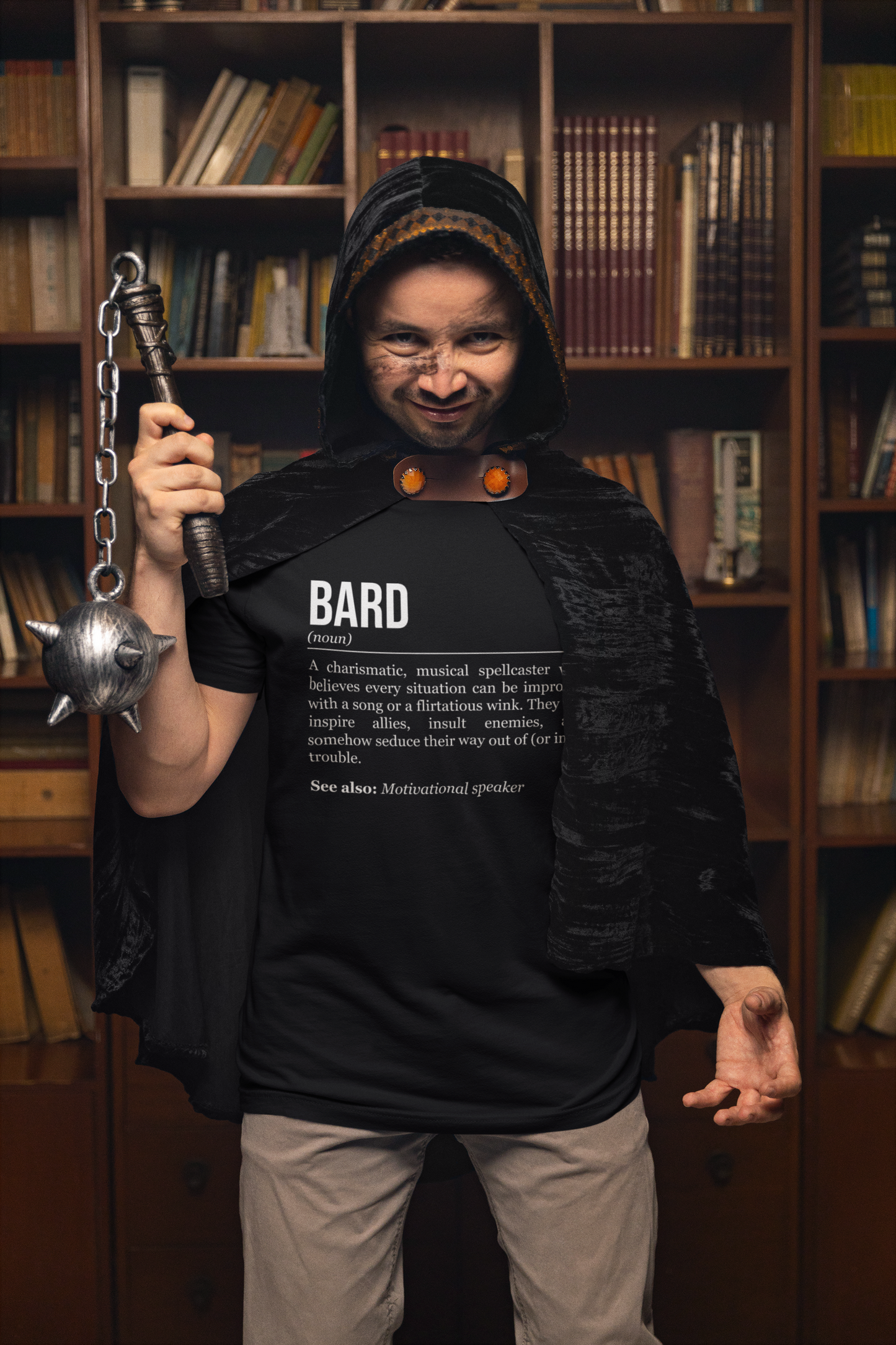 A standing man holding a morning star, wearing a cape and a black bard T-shirt showing the definition of the class Bard.