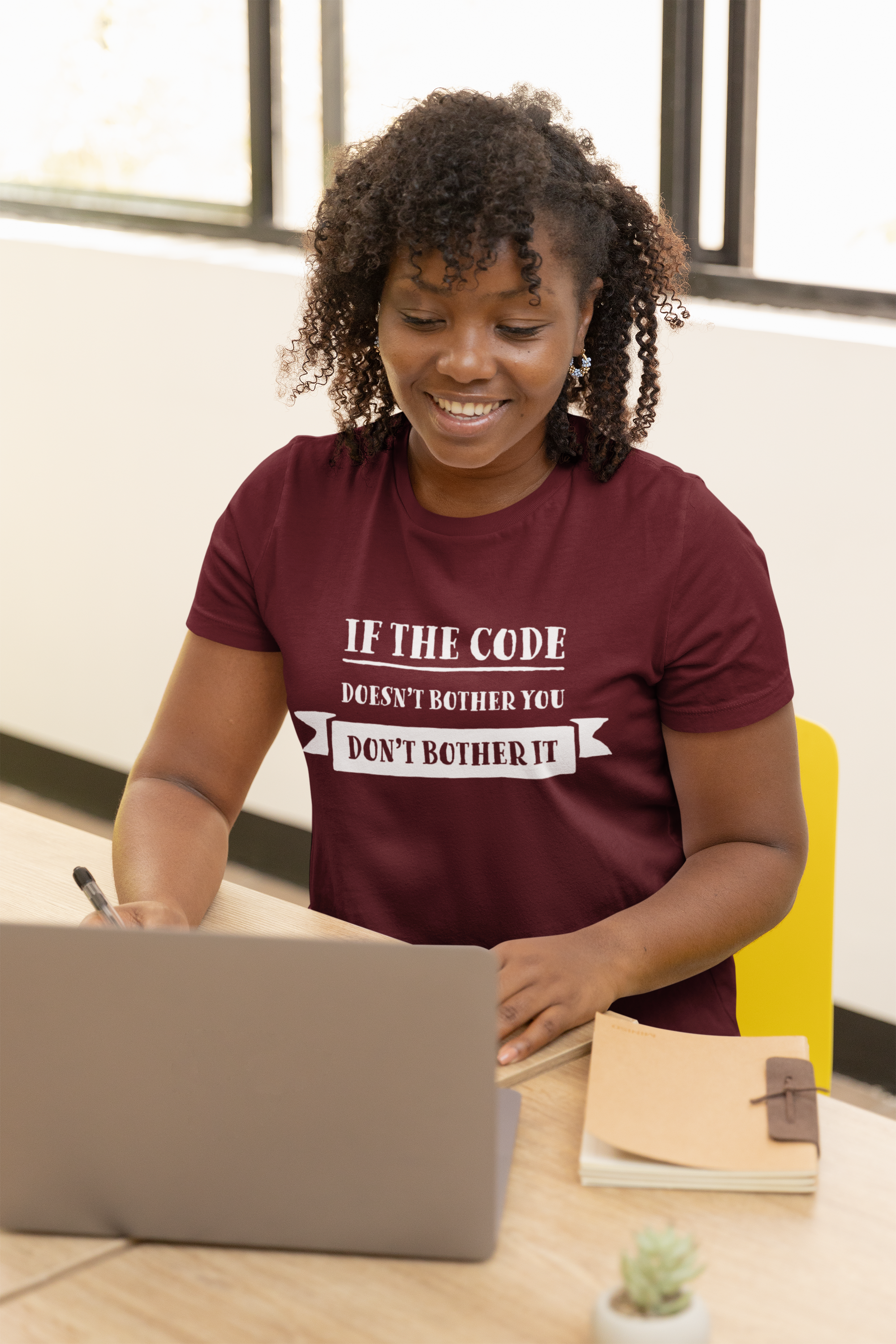 Girl working at her laptop wearing a red programming t-shirt with the text if the code doesn't bother you, don't bother it.